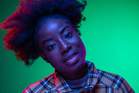 Close-up African young girls portrait on dark green studio background in purple neon light. Afro hairdo. Concept of human emotionsの写真素材