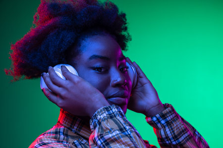 Close-up happy young girl, student listening to music in headphones isolated on dark green studio...