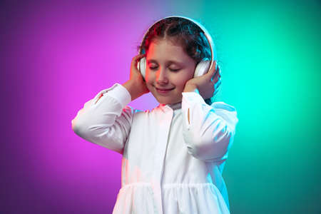 Half-length portrait of calm little girl, kid listening audio fairy-tail in headphones isolated on...