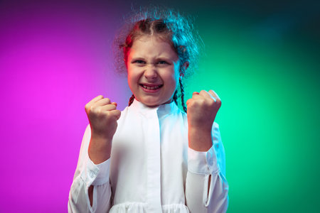 Portrait of angry little girl, kid clenches fists isolated on gradient purple blue color background...