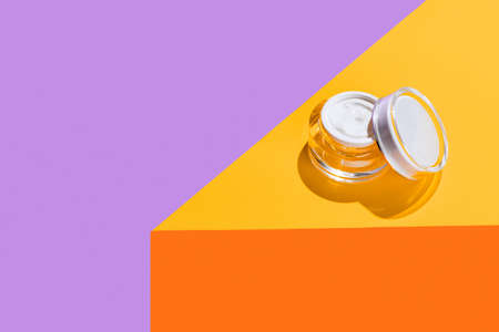 Trendy colors. Beauty and fashion. Opened glass cream pot isolated on bright colored background. Mockupの写真素材
