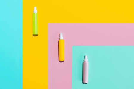 Three colored jars, spray bottles for cosmetics, cream, lotion without logos isolated over colored...