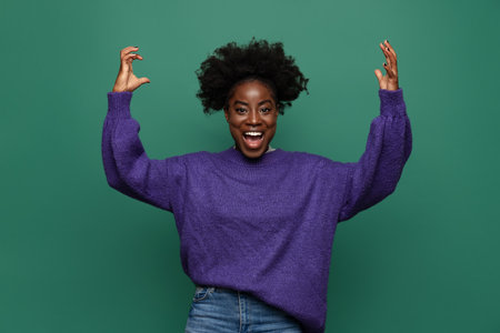 Excited African young girl standing and raising hands up isolated on dark green studio background. Concept of emotions, facial expressionsの写真素材