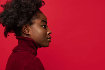 Side view of beautiful African young woman looking straight isolated on dark red studio background.の写真素材