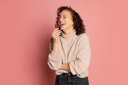 Front view of smiling young beautiful girl in warm knitted sweater isolated on peach color backgroundの写真素材