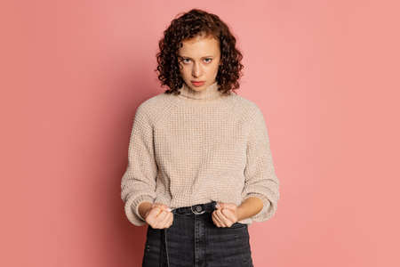 Portrait of young beautiful serious girl in warm knitted sweater isolated on coral color backgroundの写真素材