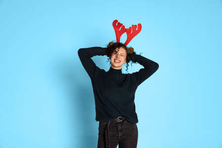 Studio shot of cute pretty cheerful young girl wearing toy deer antlers having fun isolated on blue background.の写真素材