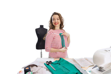 Cheerful beautiful young girl, seamstress, dressmaker working with fabric, scissors and sewing...