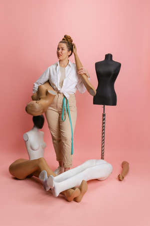 One pretty woman, seamstress tailor and parts of mannequin isolated on pink background. Concept of job, hobbyの写真素材