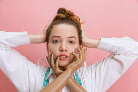 Close-up portrait of smiling girl, seamstress tailor holding mannequins plastic hands isolated on pink background. Concept of job, hobbyの写真素材