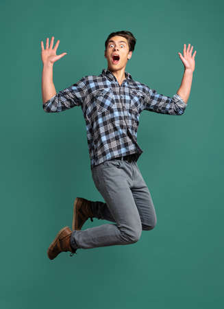 Full-length portrait of young shocked, surprised man, student jumping isolated on green studio background.の写真素材