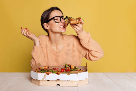 Cheerful young girl tasting Italian pizza isolated on yellow studio background. World pizza day