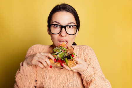Close-up young emotional girl eating Italian pizza isolated on yellow studio background. World pizza dayの写真素材