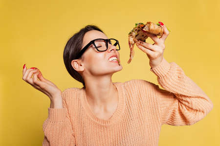 Cheerful young girl tasting delicious Italian pizza isolated on yellow studio background. World...