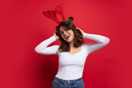 Studio shot of cute pretty cheerful young girl wearing toy deer antlers having fun isolated on red background.の写真素材