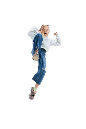 Dynamic portrait of little girl, kid in casual clothes jumping, having fun isolated on gray studio...