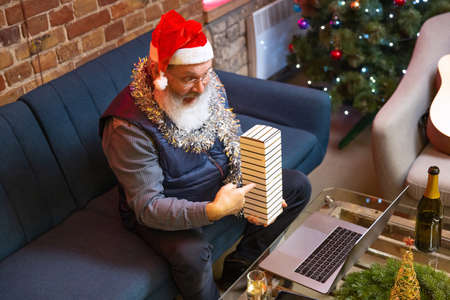 Top view of old bearded man wearing Christmas hat sitting at home and celebrates New Year with friends and family by means of video call.の写真素材
