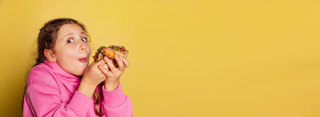 Cunning little girl, kid eating delicious pizza with cheese and tomatoes isolated on yellow studio...