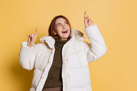 Portrait of young happy girl, student wearing warm winter coat isolated on yellow studio background.の写真素材
