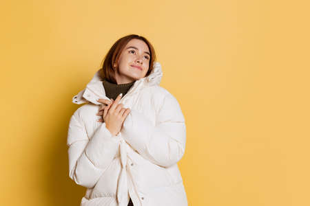 Portrait of young happy girl, student wearing warm winter coat isolated on yellow studio background.の写真素材