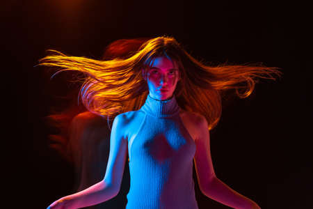 Cinematic portrait of young adorable girl with long hair posing isolated over dark background in mixed neon light.の写真素材
