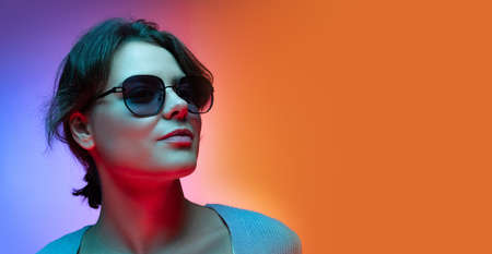 Studio shot of beautiful young girl waering sunglasses isolated on gradient blue-orange color...