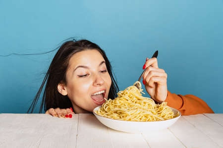 Excited young girl preparing to eat large portion of noodles isolated on blue studio background....