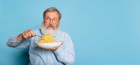Surprised senior hairy gray-bearded man eating large portion of noodles, pasta isolated on blue studio background.の写真素材