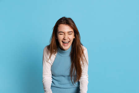 Half-length portrait of pretty girl with long glossy hair laughing isolated on blue studio backgroud. Human emotions, facial expression conceptの写真素材