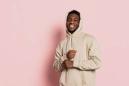 Smiling guy, young dark skinned man wearing hoodie, youth clothes isolated on pink studio background with copyspace for ad.の写真素材