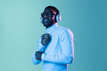 Studio shot of young fashionable guy, student wearing white neck-polo and jeans isolated on blue background in neon light.の写真素材