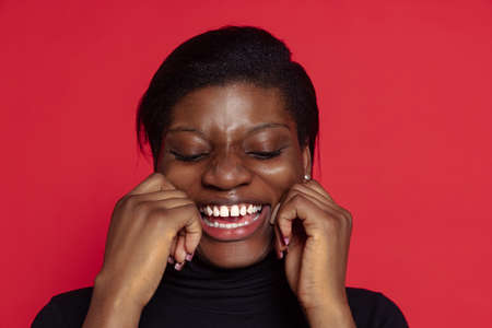 Portrait of young dark skinned girl laughing isolated on dark red studio background. Concept of emotions, facial expressionsの写真素材