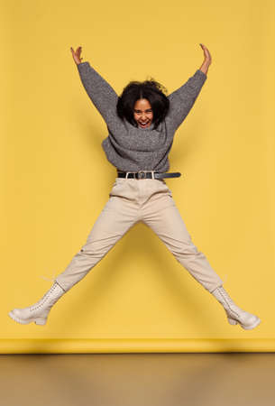 Full-length portrait of young happy dark skinned girl in warm knitted sweater jumping isolated on...