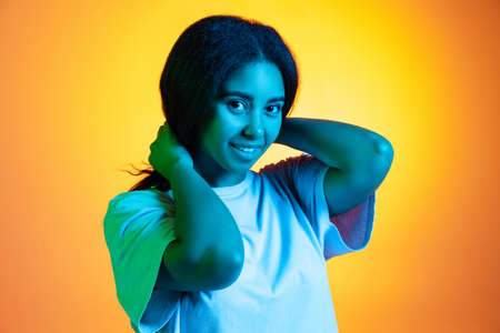 Excited young pretty dark skinned girl wearing white t-shirt isolated on yellow background in neon...