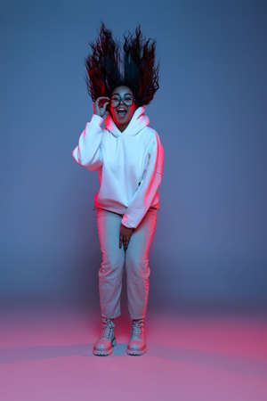 Full-length portrait of young happy dark skinned girl in hoodie jumping, dancing isolated on...