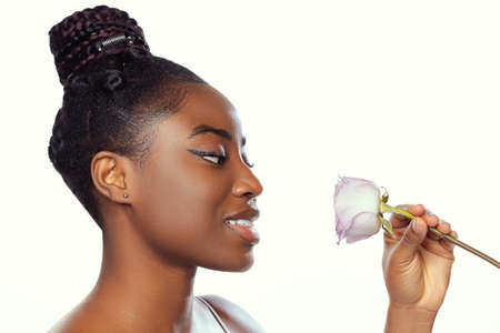 Portrait of young beautiful dark skinned woman without makeup with flower isolated over white studio...