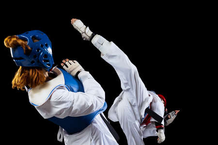 Dynamic portrait of two young women, taekwondo athletes training together isolated over dark background. Concept of sport, skillsの写真素材