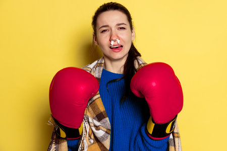 Portrait of Caucasian young woman flu and cold, feeling sick wearing boxer gloves isolated on yellow...