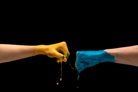 Male and female hands painted blue and yellow gesturing on dark studio backgroundの写真素材