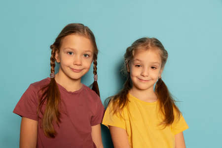 Studio shot of cute little girls, sisters or siblings wearing casual style clothes isolated on blue background. Concept of childhood, emotionsの写真素材