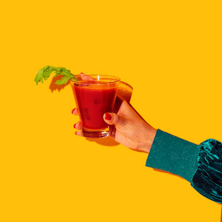 Female hand with bloody mary glass isolated on bright yellow neon background. Concept of taste, alcoholic drinksの写真素材