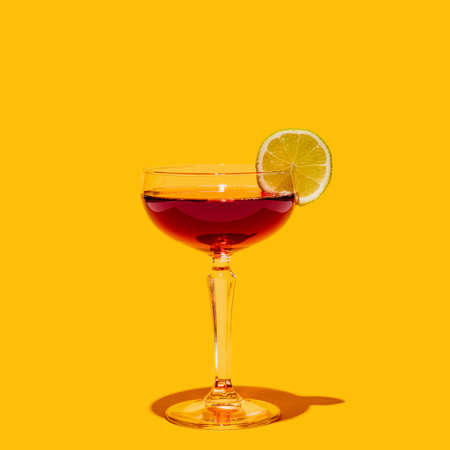 Glass with manhattan cocktail isolated on bright yellow neon background. Concept of taste, alcoholic drinks, retro styleの写真素材