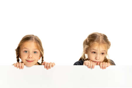 Cute little girls, sisters or siblings looking at camera isolated on white studio background. Concept of childhood, emotions, studyの写真素材