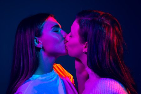 Close-up young girls, couple kissing isolated on blue background in neon light. Concept of emotions, love, relations, romantic holidays.の写真素材