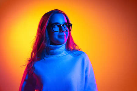 Half-length portrait of young beautiful girl isolated on orange background in neon light, filter. Concept of emotions, facial expression, youth, aspiration, salesの写真素材