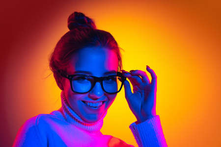Half-length portrait of young beautiful girl isolated on orange background in neon light, filter. Concept of emotions, facial expression, youth, aspiration, salesの写真素材