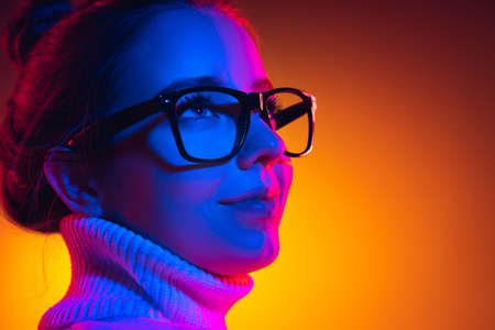 Closeup young beautiful girl in eyewear isolated on orange background in neon light, filter. Concept of emotionsの写真素材