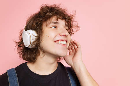 Closeup young handsome man, student in black t-shirt in headphones isolated on pink background....