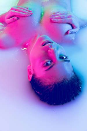 Sensual young girl in the milk bath with soft glowing in blue-pink neon light. Copyspace for...