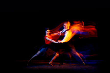 Dynamic portrait of young ballroom dancers dancing Argentine tango isolated on dark background with neon mixed light.の写真素材